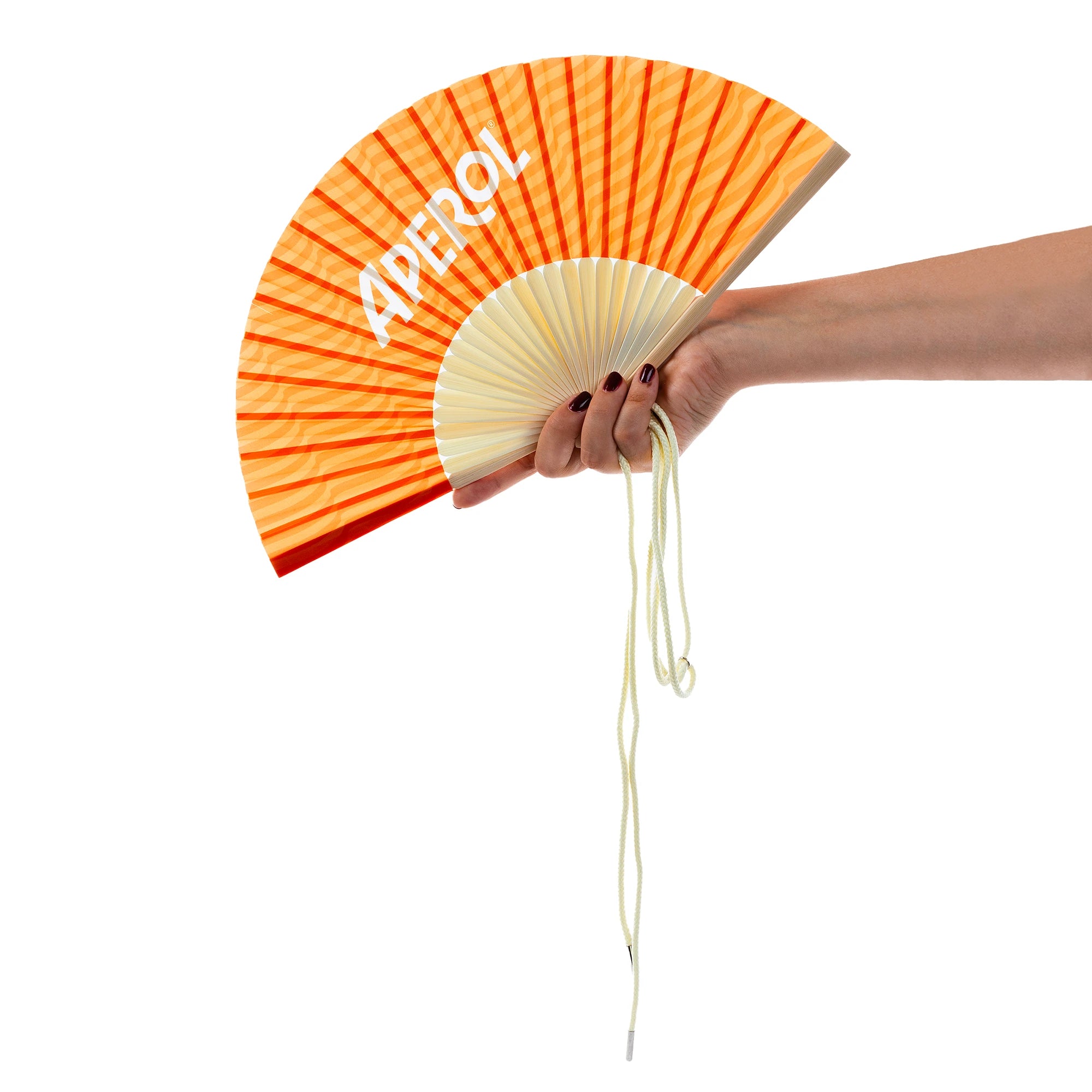 A hand holding an Aperol-branded folding fan with vibrant orange and red stripes, featuring a white Aperol logo and a cream-colored string hanging below, set against a clean white background.