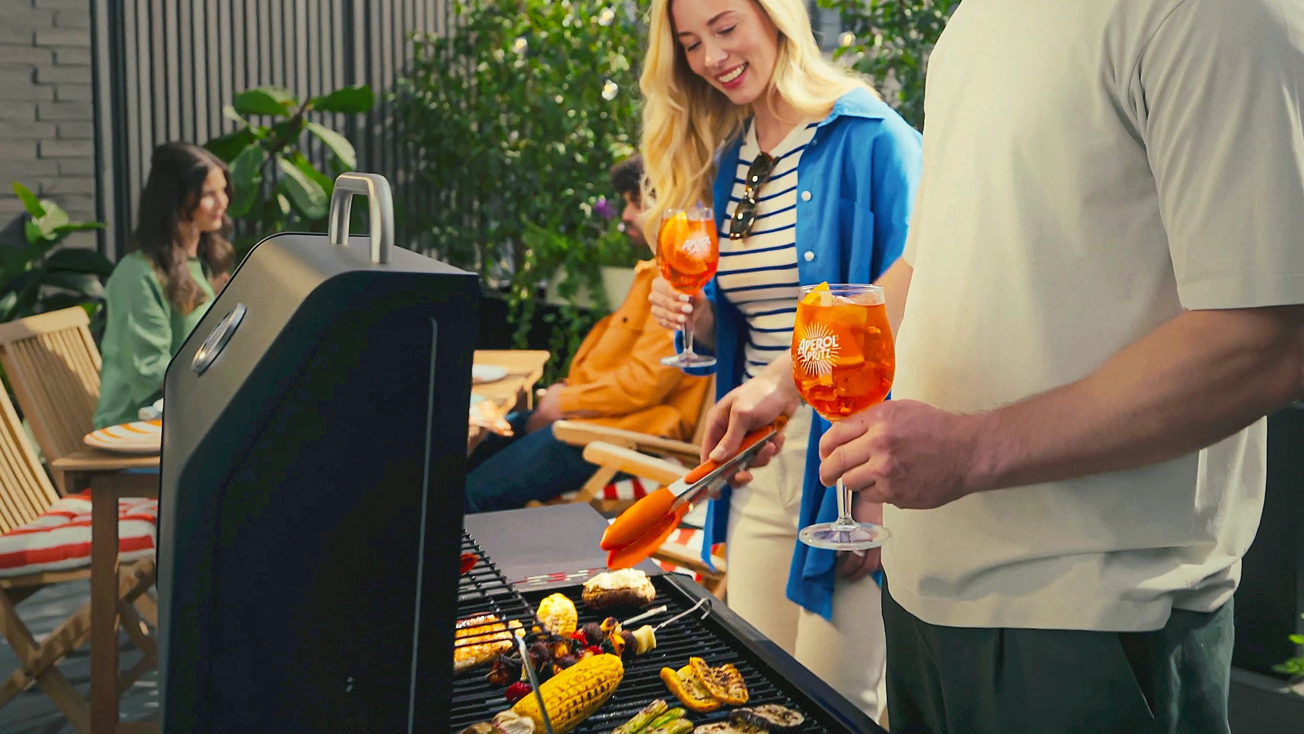 Group enjoying outdoor barbecue with Aperol Spritz cocktails, grilled vegetables, and friendly atmosphere
