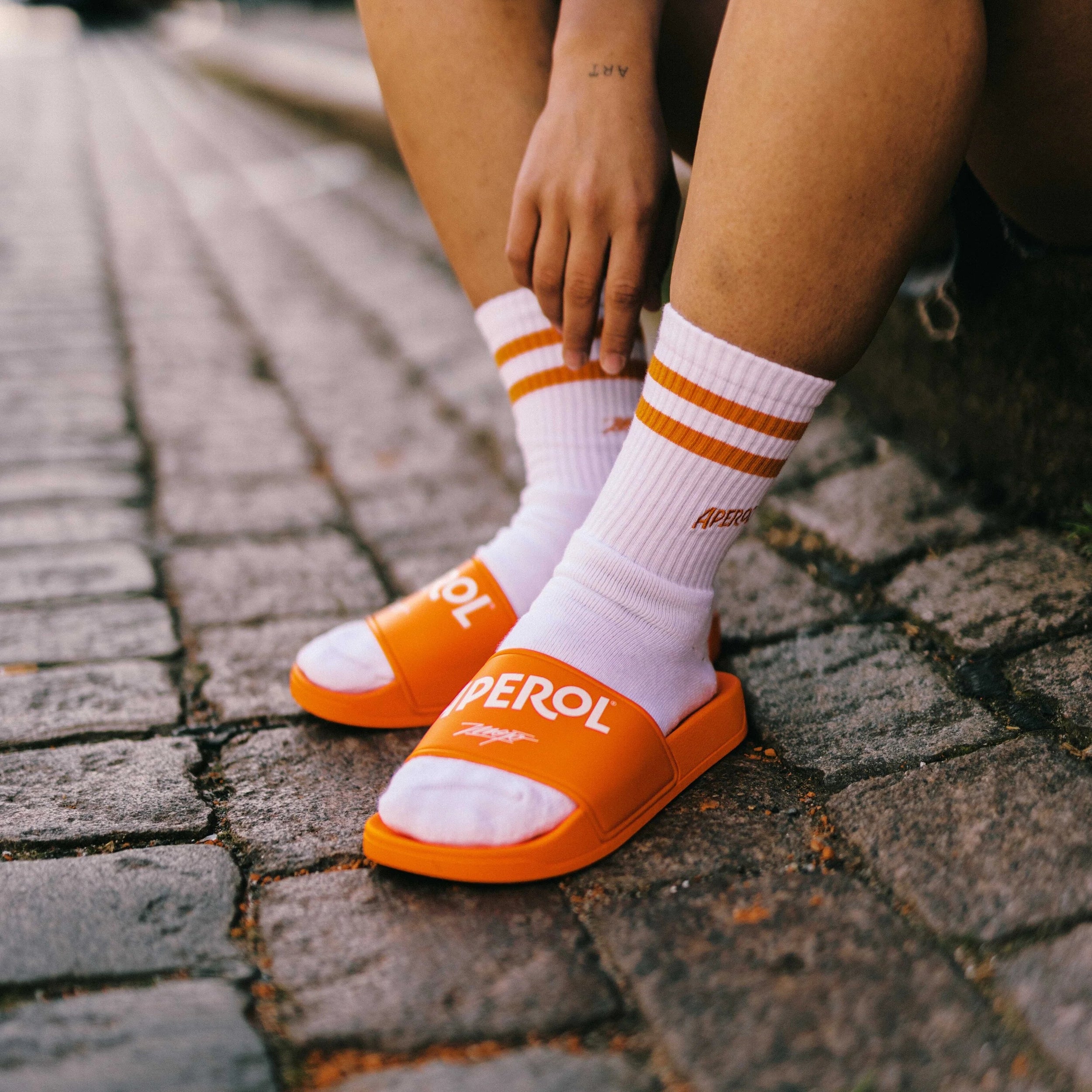Person wearing orange slides with white socks on a cobblestone street