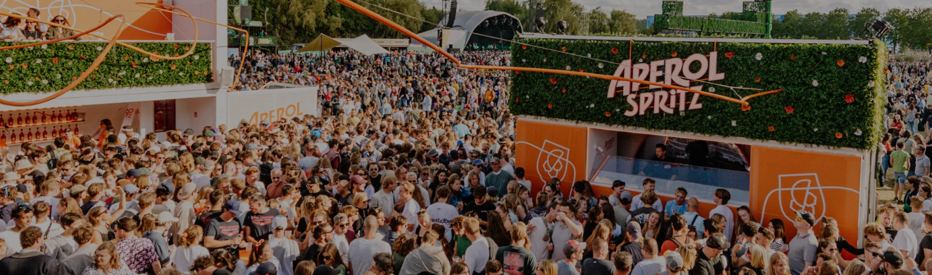 Aperol Spritz pop-up bar at a vibrant outdoor festival, surrounded by a massive crowd enjoying the lively atmosphere, music, and cocktails under a sunny sky.