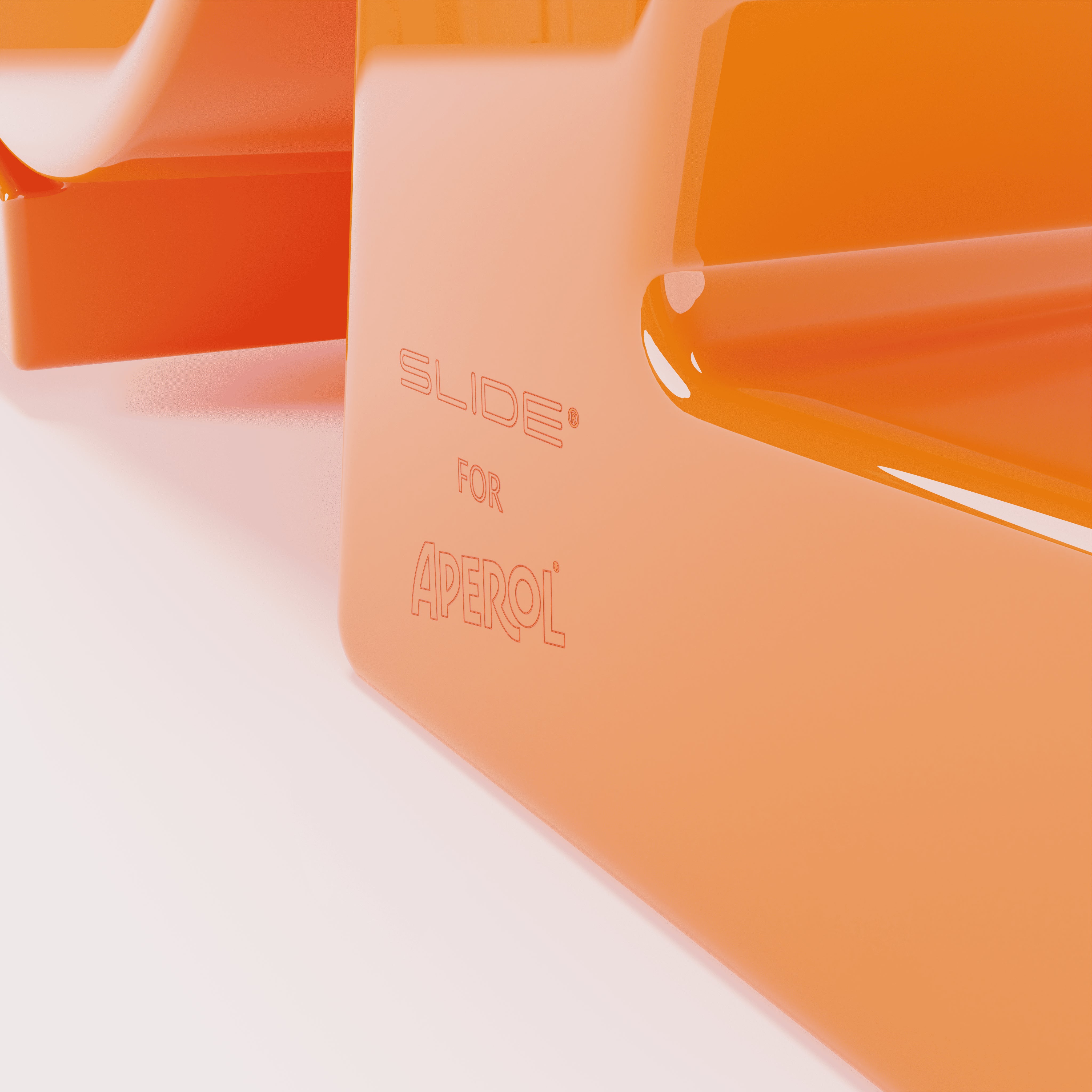 Close-up of a glossy orange surface with the engraved inscription “SLIDE® FOR APEROL®,” suggesting a designer object or furniture made for the Aperol brand.