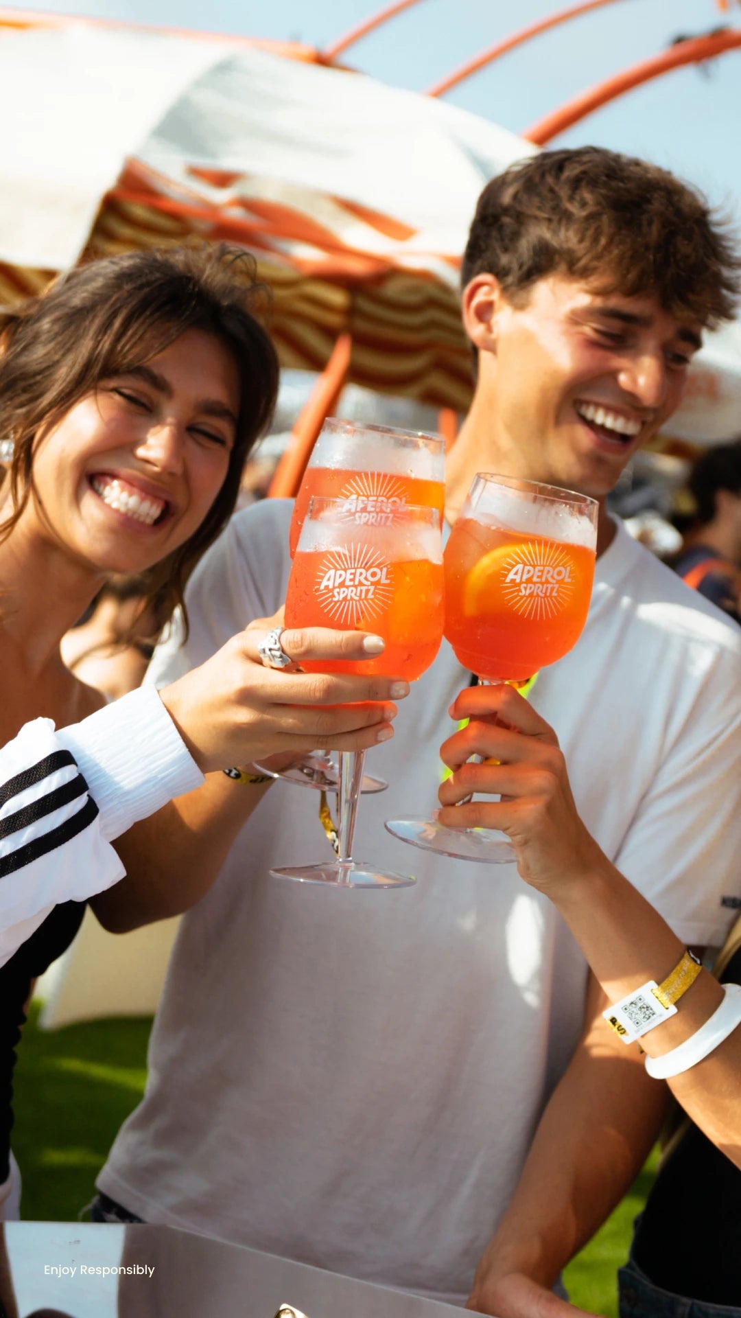 Friends cheering with Aperol Spritz cocktails at a sunny outdoor event, smiling and enjoying the moment
