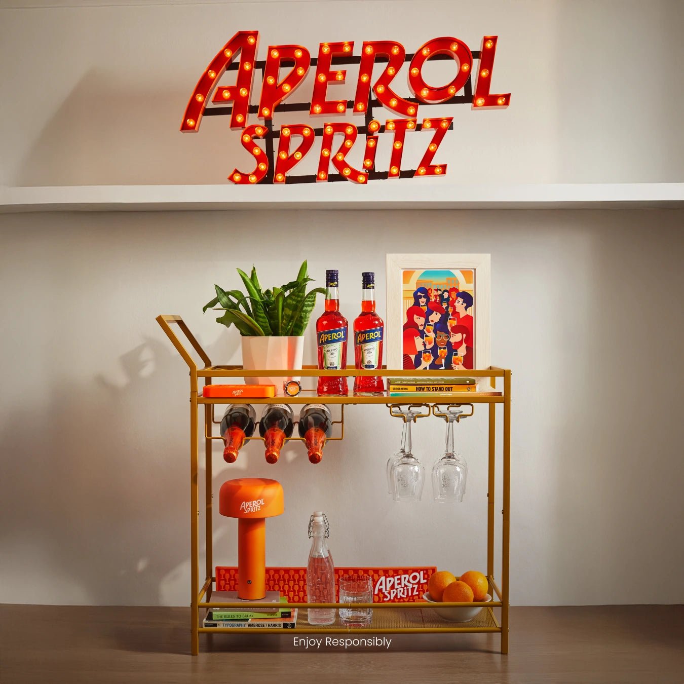 Aperol-themed bar cart with bottles, glasses, and accessories under a light-up Aperol Spritz sign