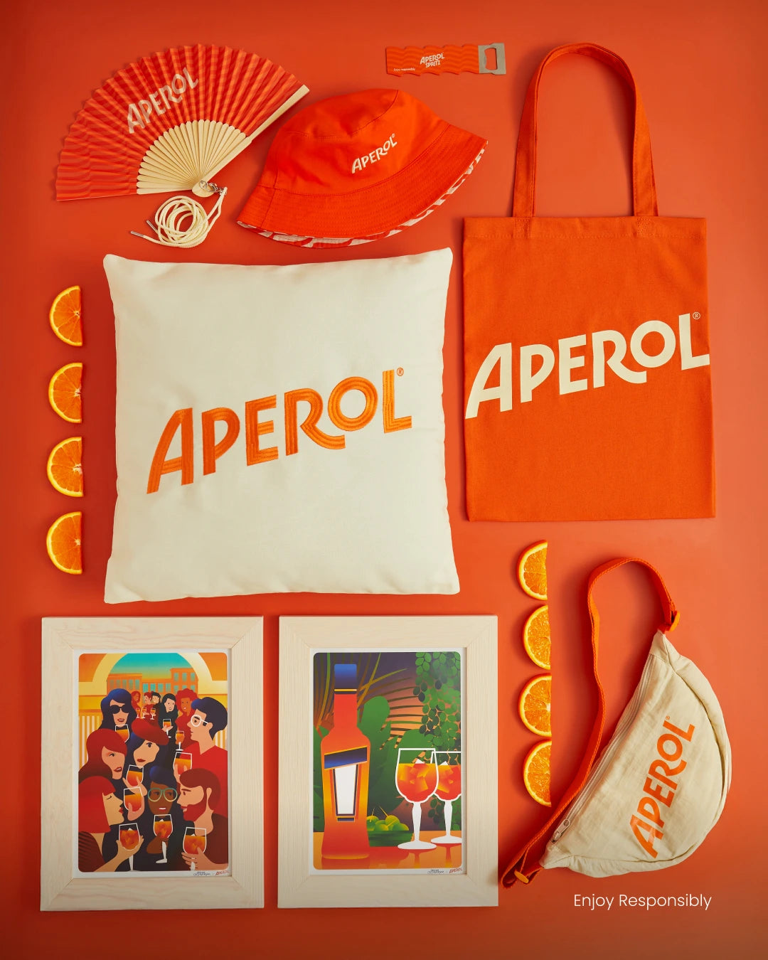 Collection of Aperol-branded products including a tote bag, hat, fan, and posters on an orange background.