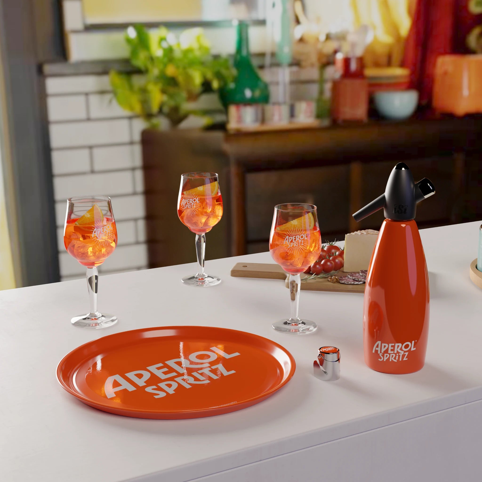 Aperol Spritz setup on a kitchen counter featuring an orange Aperol-branded tray, three filled spritz glasses, a soda siphon, and a wooden board with cheese, cherry tomatoes, and salami, with a cozy, warmly lit kitchen in the background.