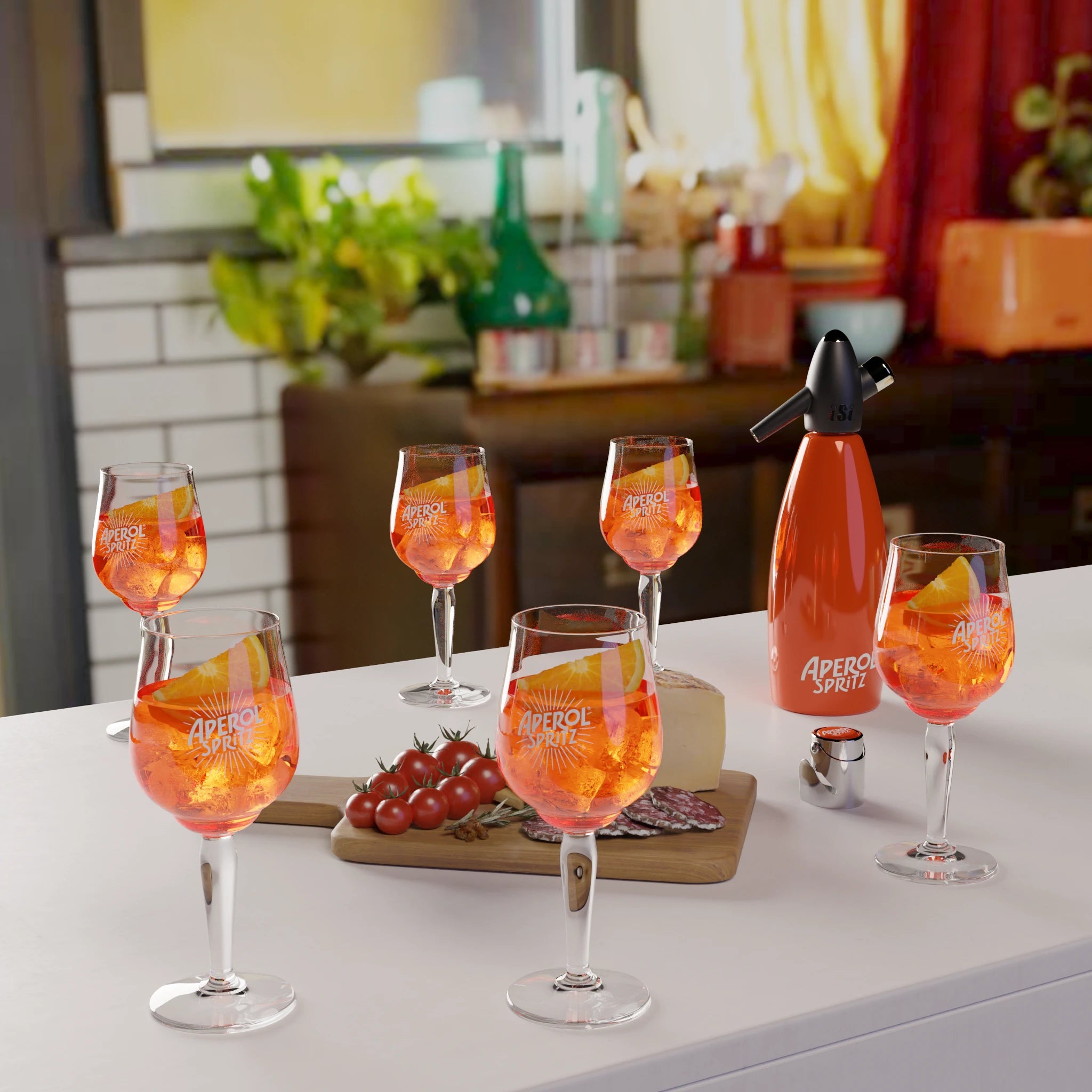 A kitchen counter scene with six glasses filled with Aperol Spritz, an orange siphon labeled "Aperol Spritz", and a tasting board with cherry tomatoes, salami slices, and a piece of cheese. In the background, a cozy retro-style kitchen with plants.