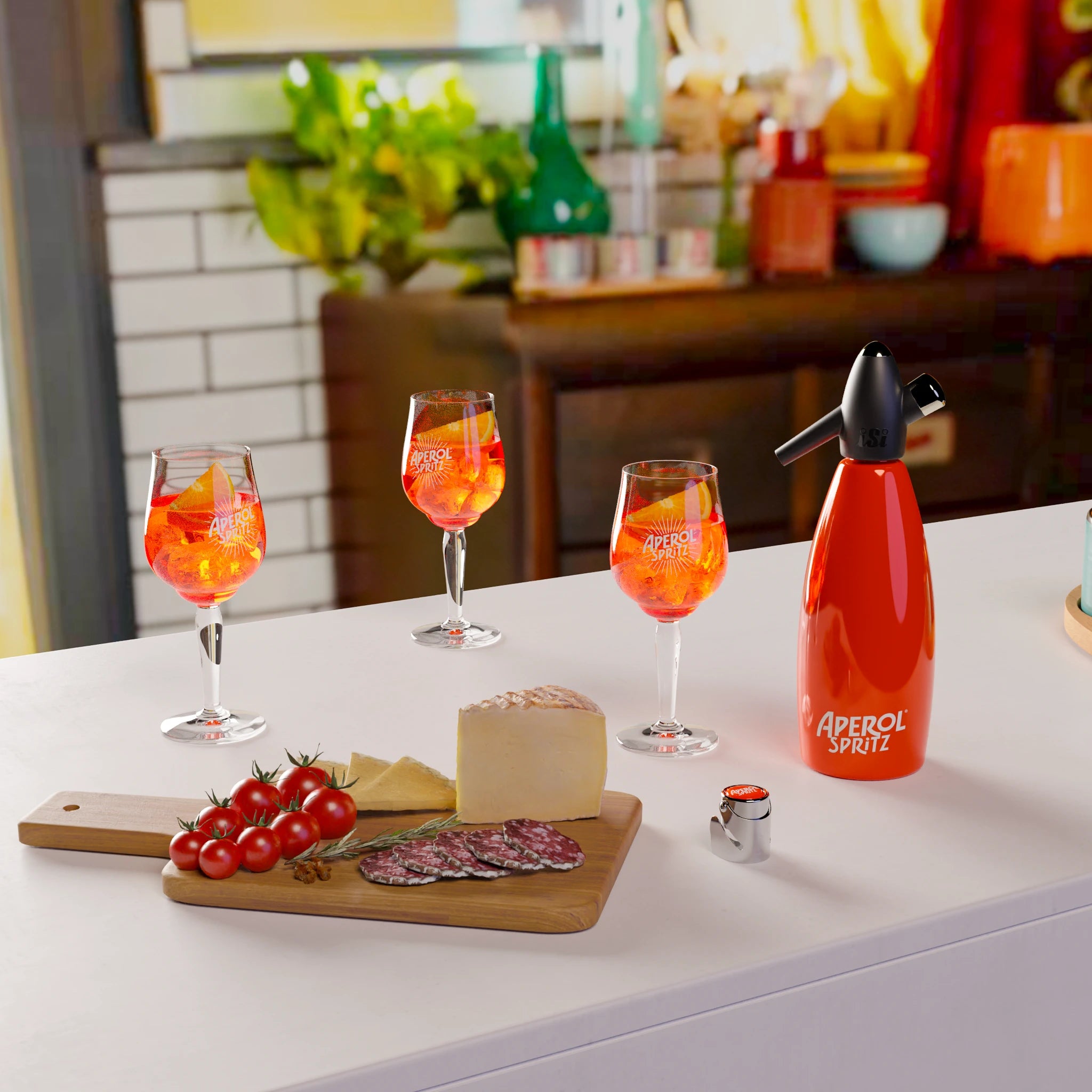Aperol Spritz prep scene: three stemmed glasses filled with Aperol Spritz and orange slices on a white countertop, alongside an orange “Aperol Spritz” soda siphon and a chrome bottle stopper with an orange top, with a charcuterie board and blurred kitchen setting in the background.
