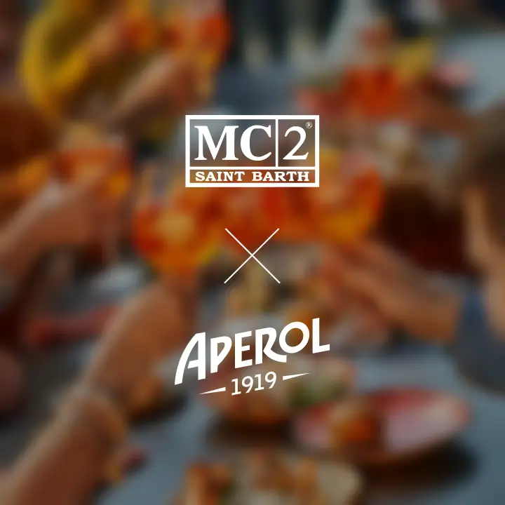 Blurred background of friends toasting with Aperol Spritz glasses at a festive table; overlaid with logos of MC2 Saint Barth and Aperol 1919.
