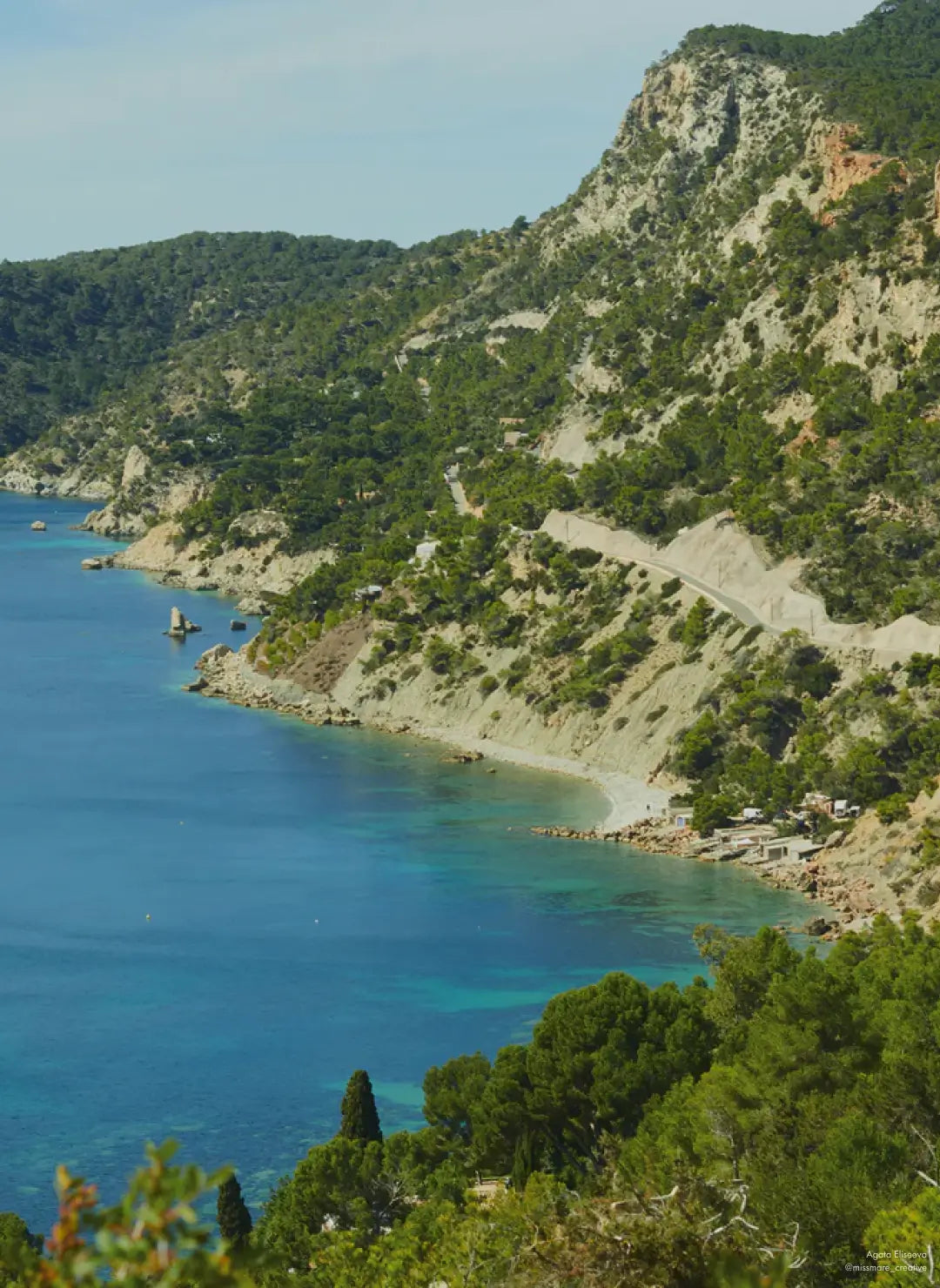 Scenic coastal view of a winding road along lush, green cliffs meeting the calm blue waters of the sea in St. Barth.