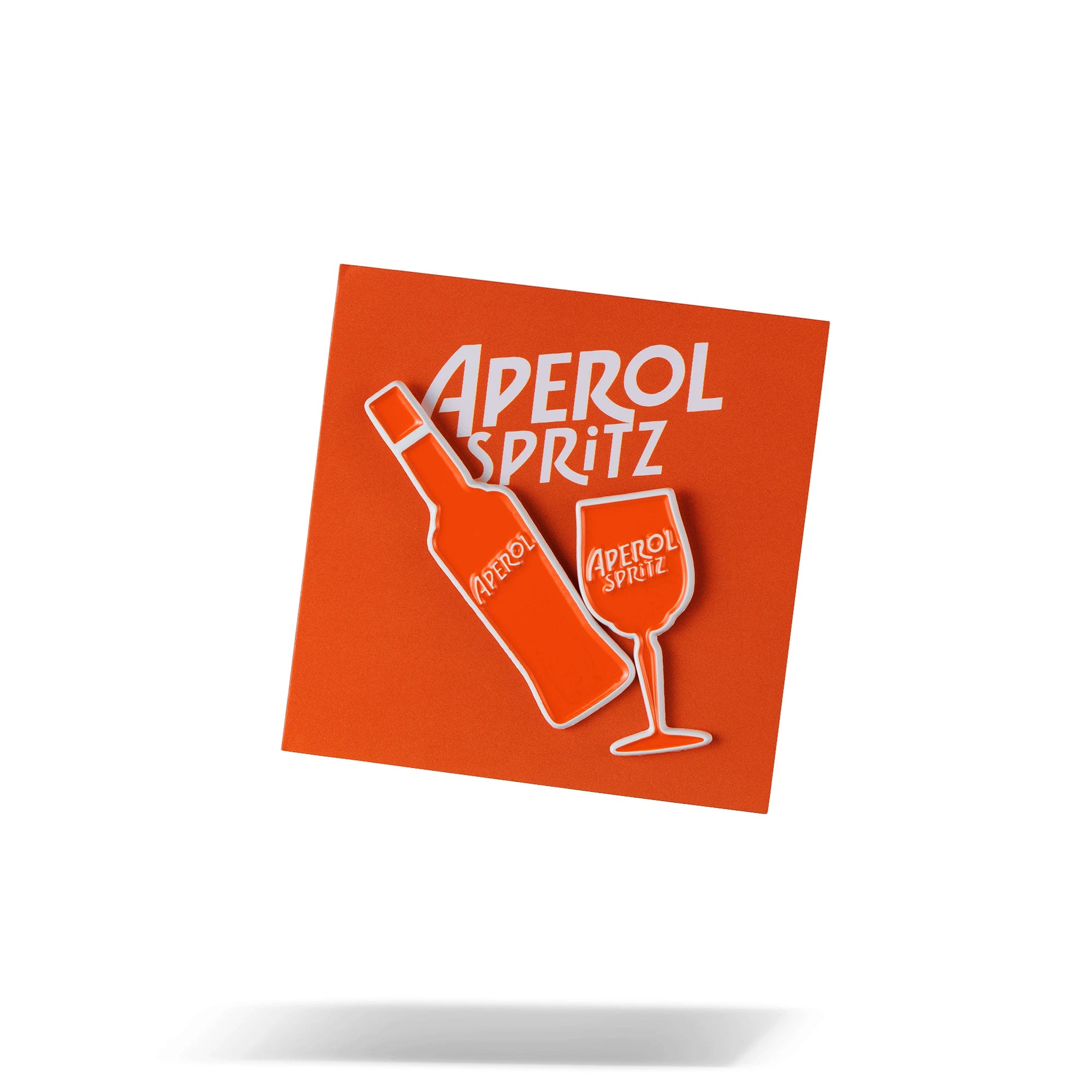 Set of two Aperol Spritz enamel pin badges — one shaped like a bottle and the other like a wine glass — displayed on an orange backing card with bold white Aperol Spritz branding.